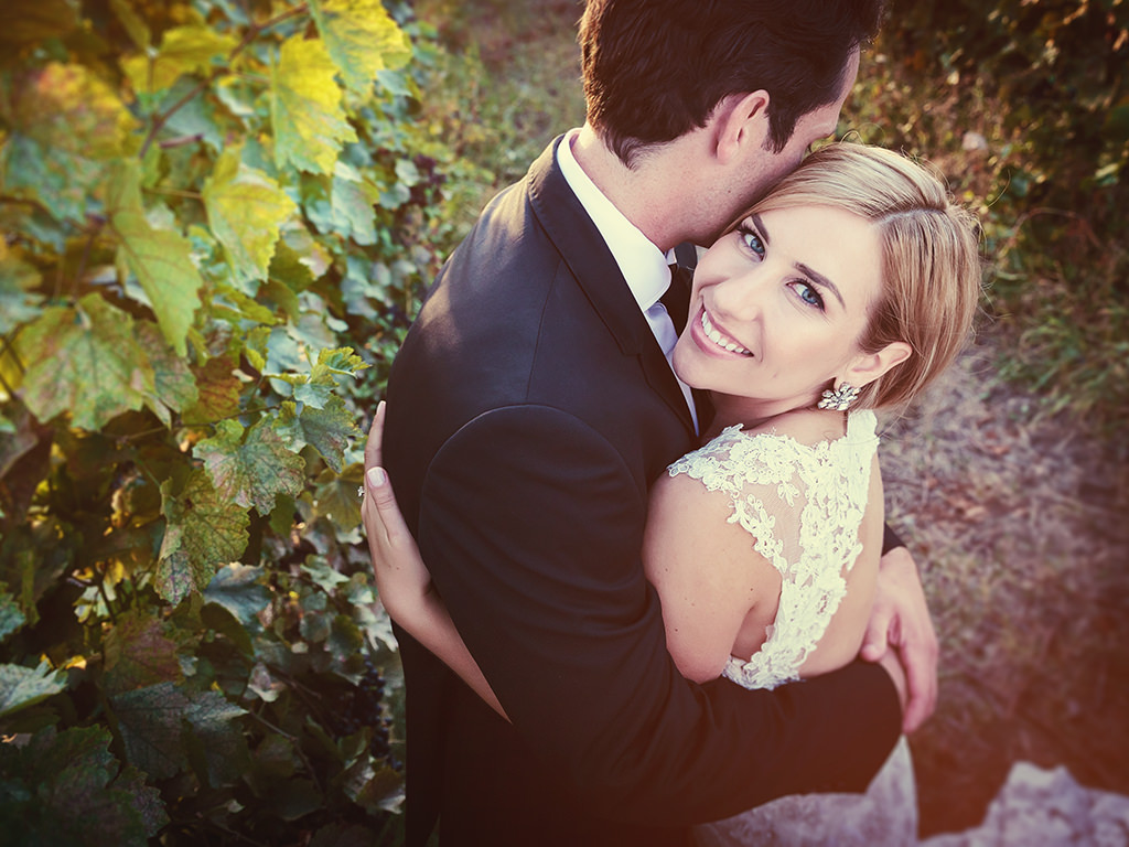 A bride and groom hug in a vineyard at Summerhill Pyramid Winery during sunset.