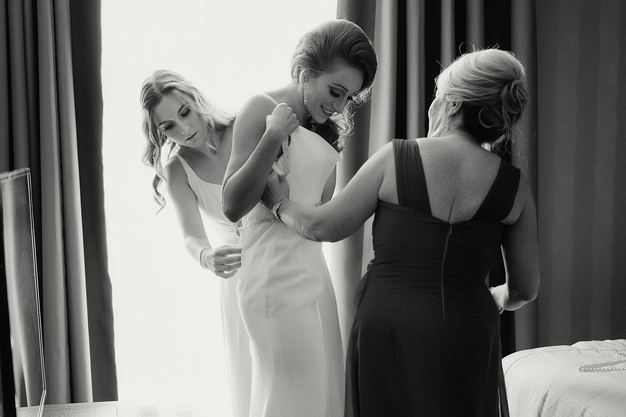 A bride is helped into her wedding dress by her mother and sister.