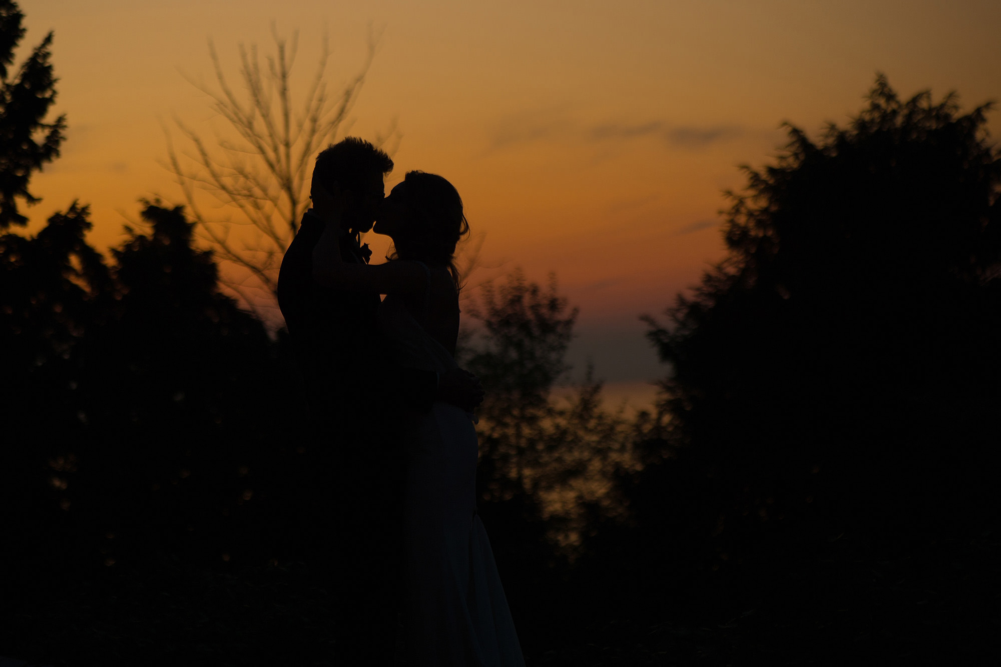 Silouette of bride kissing her husband at sunset.