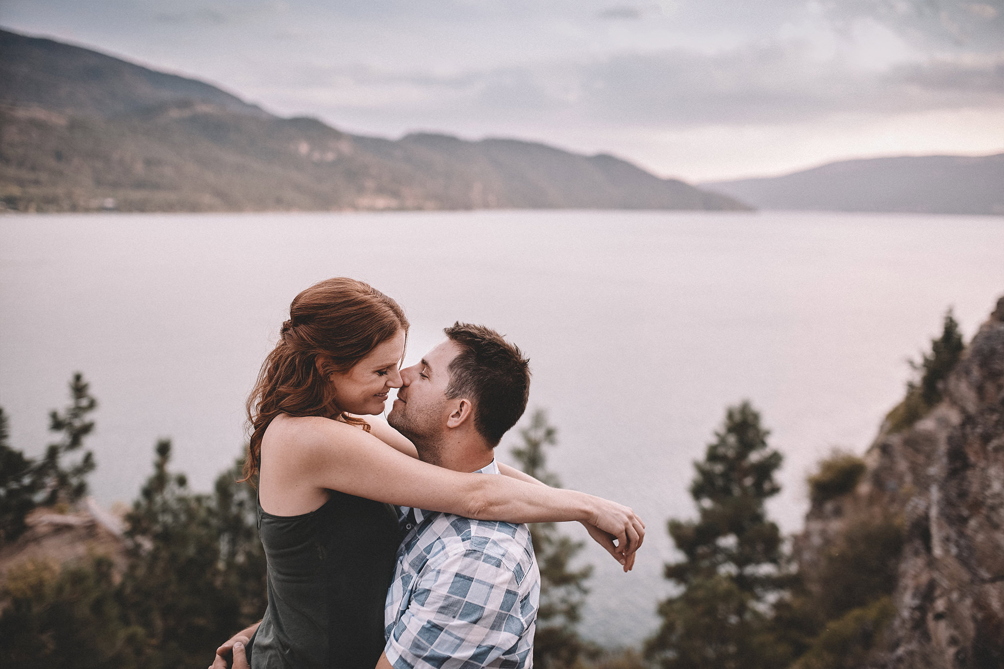 A couple hold each other and kiss with a big lake in the background